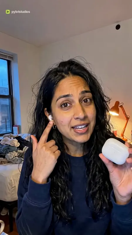 A presenter at home pointing to her ear while holding an Orrin earbuds case, poster frame from the Orrin earbuds sample advert
