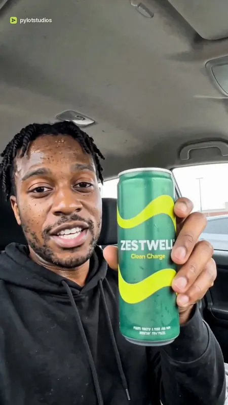 A presenter in a parked car holding up a green Zestwell can, poster frame from the Zestwell energy drink sample advert